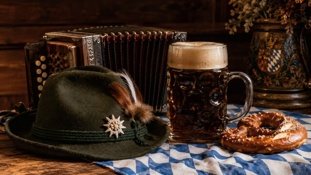 Traditional Bavarian Oktoberfest still life with alpine hat accordion beer stein and pretzel on blue checkered cloth