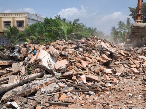 Excavator clearing piles of building rubble at a demolition site