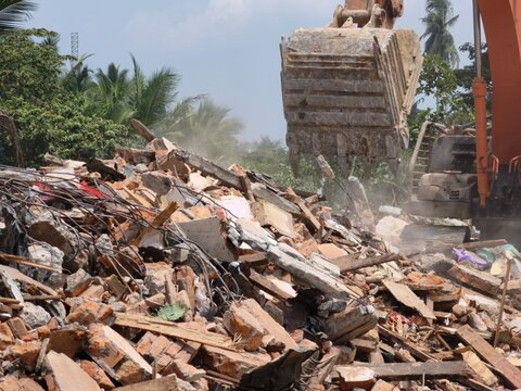 Excavator tearing down old building structure amidst dust and debris