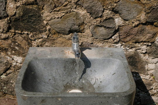 Outdoor concrete sink basin with a running water faucet against a stone wall. Ideal for sanitation, hygiene, architecture, and utility concepts
