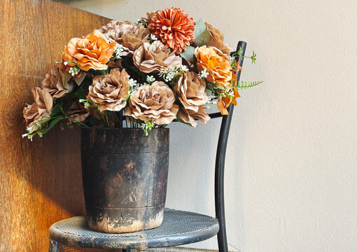 Vintage bouquet of autumn roses in a rustic wooden pot on a chair, featuring ample copy space on the right wall for text placement.