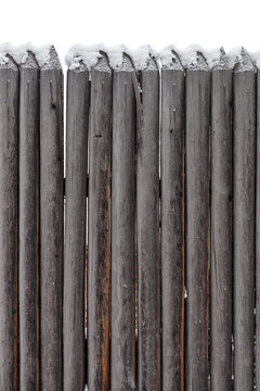 Close up of wooden fence with pointed tops covered snow in winter season, old rustic border against white background. Vertical wood palisade with round tree sharp logs, timber textured wall.