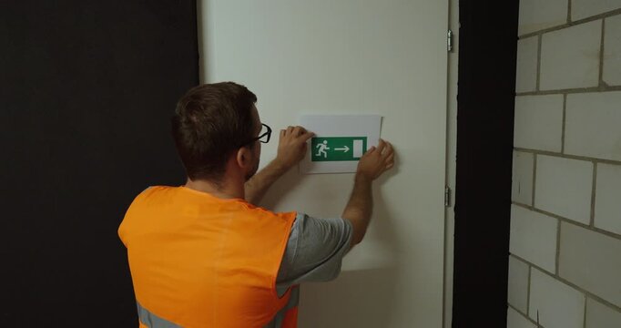 Worker installing an emergency exit sign on a door. Ideal for workplace safety, evacuation routes, emergency preparedness, and building compliance concepts.