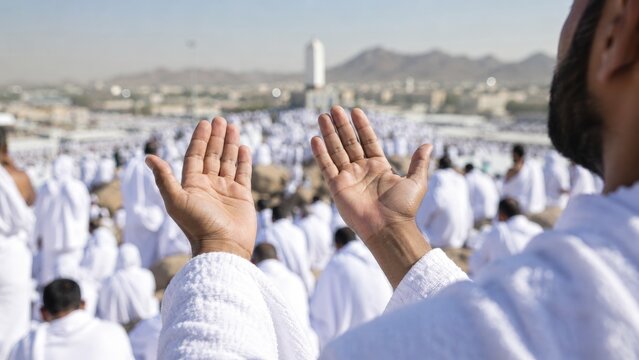 Pilgrims in white ihram robes raising hands in supplication during the Hajj pilgrimage at a large outdoor religious gathering