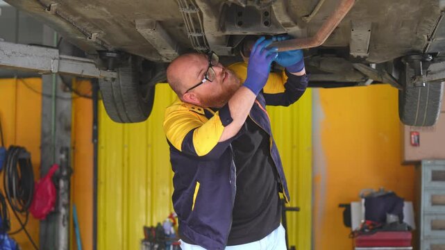 Automotive technician performing maintenance on a car while surrounded by various tools and equipment in a workshop