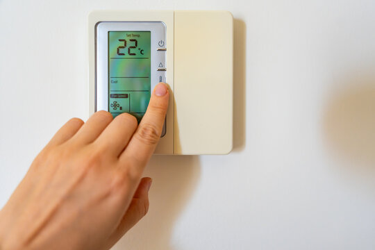Hand adjusting a digital thermostat set to 22 degrees on a modern wall mounted climate controller. Smart home technology, indoor comfort and energy efficient temperature control.