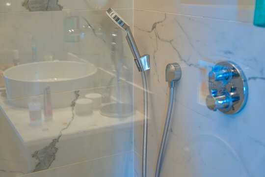 Modern walk in shower with glass partition, handheld showerhead and marble wall tiles. Contemporary bathroom design, hygiene and comfortable daily living.