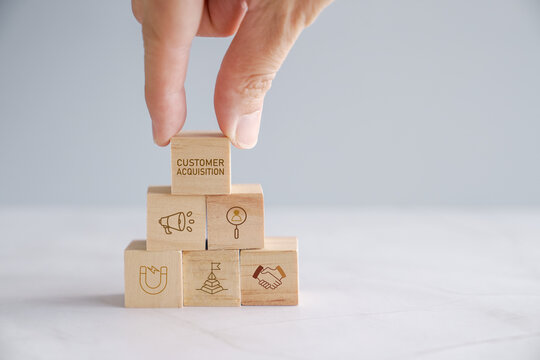 Hands holding wooden blocks with Customer Acquisition, business marketing strategies and processes to gain new clients.