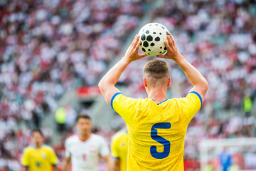 Fototapeta premium A soccer player wearing a yellow jersey with number 5 holding a ball over his head to perform a throw-in during a stadium match.