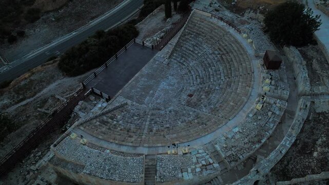 Top-down aerial view of Kourion Ancient Amphitheater in Cyprus. The curved stone seating and theatre layout create a striking ancient architectural pattern.