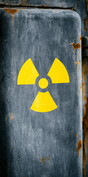 A weathered metal surface displaying a bright yellow radiation warning symbol. The texture of the metal shows signs of age and rust, adding a sense of danger and caution