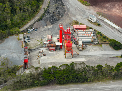 Aerial view of an industrial facility with red silos, storage tanks, and gravel piles surrounded by lush greenery in Sao Miguel, Acores, Portugal.
