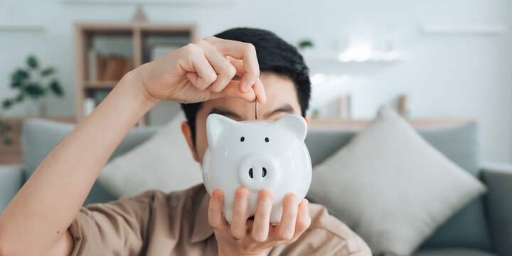 Hand of young Asian man putting coin in piggy bank. Save money and financial investment