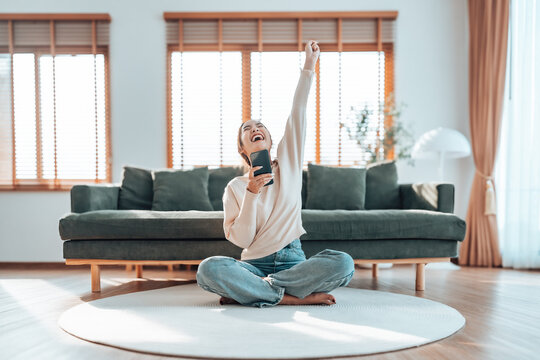 Smiling pretty young Asian woman sitting on cozy couch, using funny mobile apps in living room. Woman at Home, Doing Online Shopping, Messaging Friends, Posting on Social Media