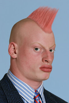 people of ai, yearbook photo of a person with pink mohawk with shaved sides, stern side-eye pout, dark pinstripe suit with blue striped shirt and red tie, photorealistic.png