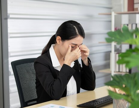 Tired Asian businesswoman rubbing her eyes from eye strain and fatigue while working at office desk