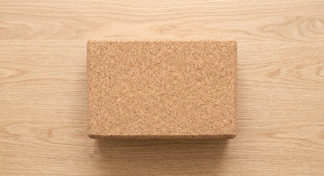 Top view of a single cork yoga block on a light wooden background providing support and stability for various yoga poses and exercises