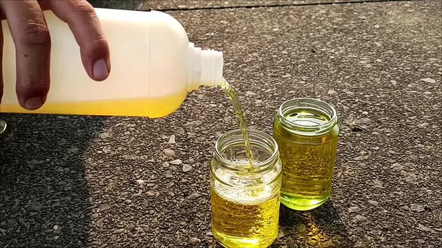 Close-up of a hand pouring golden aviation fuel into a transparent glass jar for fuel sampling and quality inspection. The image represents aircraft maintenance, fuel testing and contamination check