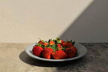 Fresh ripe strawberries on the little grey or gray plate, close up view. background. red. green leaves, leaf. health. sunlight, sunshine. black, dark, shadows. side. front. copy space, empty, free © Muhammad
