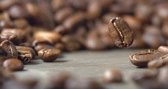 One roasted coffee bean falling onto wooden table in super slow motion