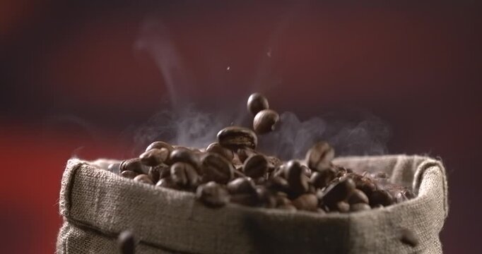 Roasted coffee beans falling into a burlap sack with rising steam in slow motion