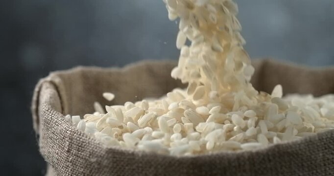 White rice grains falling into burlap sack in super slow motion