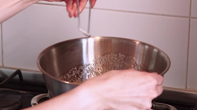Cooking meal. Whisking process. Chef hand stirring liquid frothy ingredient in stainless steel bowl with spring tool on hot stove.