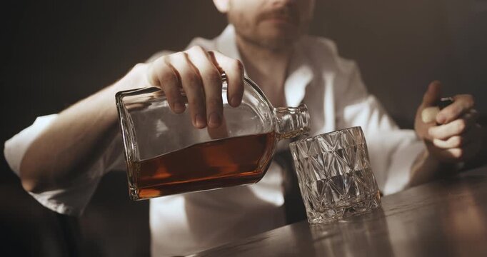 Man fills a patterned glass with liquor from a bottle and later consumes the alcoholic drink.