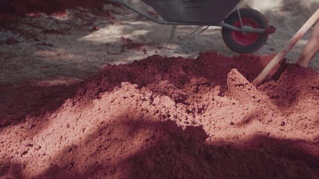 Close-up of a barefoot worker standing beside prepared red clay used for traditional wattle and daub construction in Brazil. Documentary view of natural materials, manual work and vernacular building
