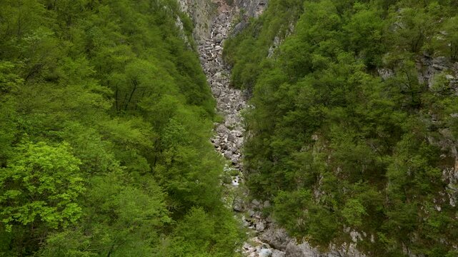 Aerial establishing of Boka Waterfall gorge surrounded by lush forest near Bovec, tilt along boulder field to water