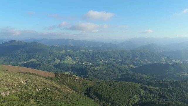 Aerial pan left reveals the lush, hilly landscape of Nouvelle-Aquitaine, France. Serene Pyrenees mountain range with scattered farmhouses.