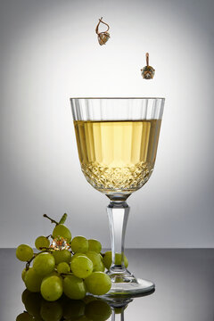 White wine with grapes and earrings falling into the wine and a ring against a dark background with reflection.