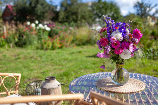 Close up of flower arrangement put on glass table in summer garden. Lounge zone with furniture and bouquet of fresh blooms in vase