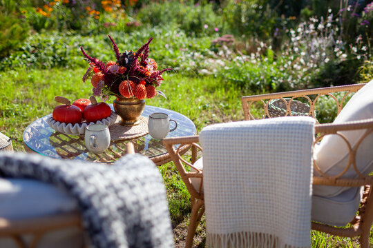 Cozy outdoor spot with furniture in autumnal garden. Table arranged with bouquet of fall flowers, orange pumpkins and coffee 