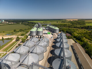 Elevated perspective of modern agricultural grain storage facility showing rows of metallic silos built near rural countryside landscapes under blue sky. © Pasha