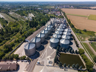Wide angle elevated perspective of large agroindustrial grain storage plant with metallic silos built near rural fields under blue sky. © Pasha