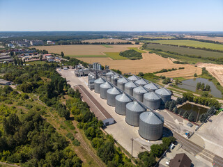 Wide angle elevated perspective of large agroindustrial grain elevator plant with metal silos built near countryside fields on sunny day. © Pasha