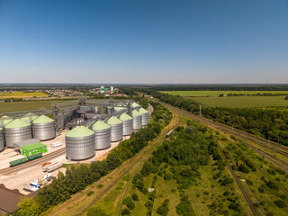Wide angle elevated perspective of large agroindustrial grain storage facility featuring green roof silos next to multiple railroad tracks. © Pasha