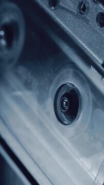 Vertical macro shot of a compact cassette hub spinning inside a tape deck. Close up of magnetic tape, transparent shell and reel motion in retro analog audio equipment