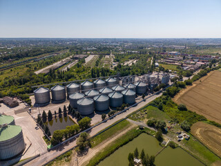 Elevated perspective of modern industrial agroindustrial storage complex showing numerous metallic silos built near countryside reservoirs. © Pasha