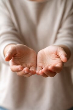 Open hands of a person with light skin, palms facing up, positioned in front of a neutral background, suggesting offering or receiving something