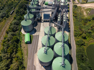 Elevated viewpoint of agricultural storage facility featuring metallic silos with green roofs built next to railway tracks. © Pasha
