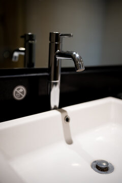 Modern chrome water faucet mounted on a clean white bathroom sink basin with soft blurred background bokeh