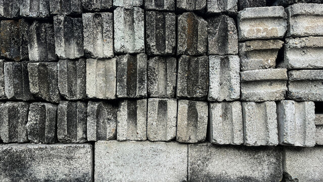 Stacked concrete blocks form a textured, weathered wall. Gray tones and rough surfaces suggest aged construction. Each block shows signs of wear, exposure, and time. Suitable for backgrounds. side
