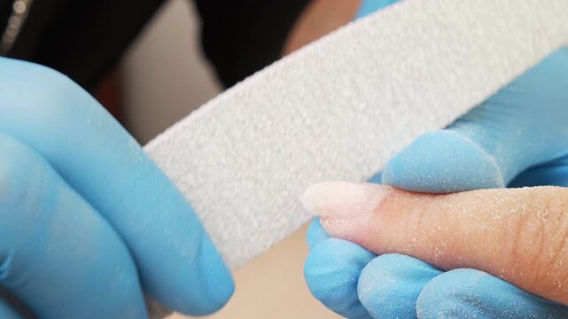 Manicurist files the shape of the nails with a special nail file, close up view. The manicurist shapes the nails with a nail file. The process of nail care in a beauty salon. Nail file processing.