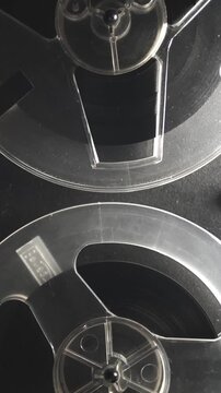 Vertical close up of a reel to reel tape recorder with two transparent spools of magnetic tape rotating. Retro analog audio equipment for vintage sound and archive footage
