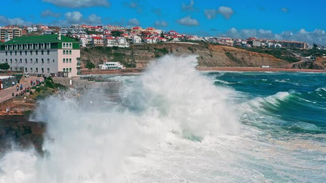 Ocean waves crashing. Beautiful touristic Ericeira city on summer sunny day during sunset. Large ocean waves crash about the  pier - real time. Big waves is  crashing on rock creating huge splashes.