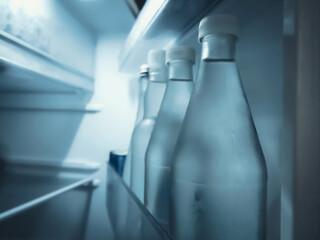 Chilled glass water bottles standing inside a dark home refrigerator © Win Nondakowit