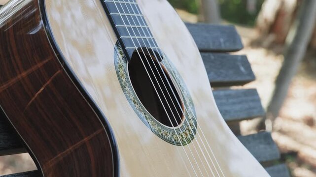 Guitar body of a classical wooden guitar with white top. Part of a classical guitar on a blurry background, outdoors.   Close-up guitar body with beautiful rossete. Slow motion panning of   guitar.