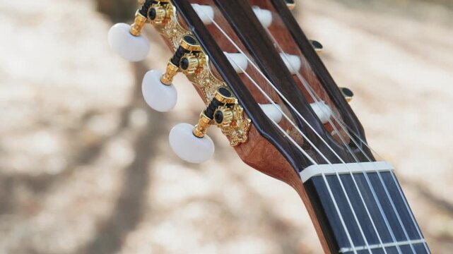 Close-up of the guitar head of a classical guitar with gold pegs. Part of a classical guitar on a blurry background in the park. Head of guitar with nylon strings. Slow motion 4k footage.
